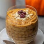 "Two mason jars filled with creamy pumpkin overnight oats topped with crushed graham crackers, sitting on a rustic wooden table with fall-themed decor like mini pumpkins and cinnamon sticks in the background."