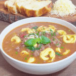 A hearty bowl of Crock-Pot Olive Garden Pasta e Fagioli copycat recipe, garnished with fresh parsley, with breadsticks alongside.