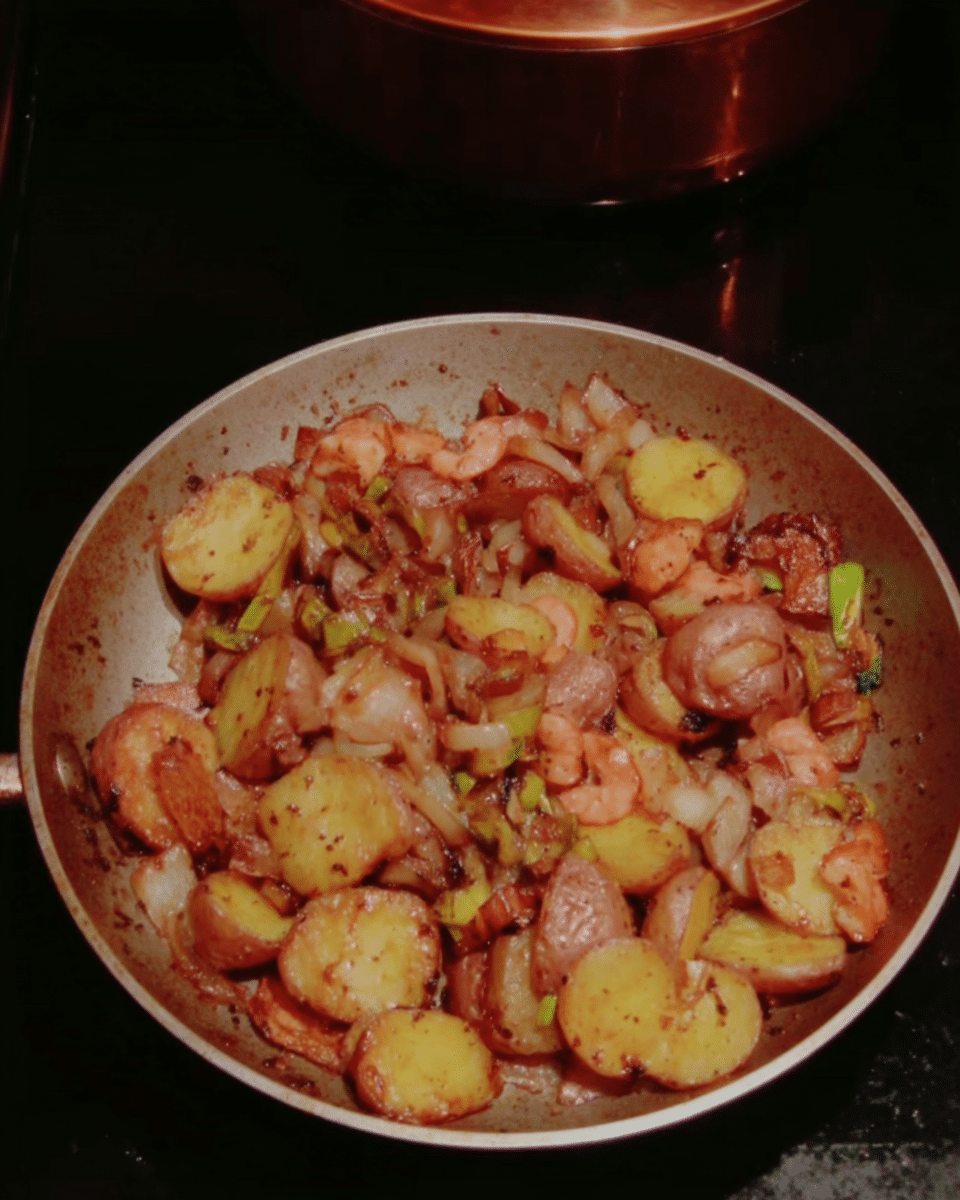 An array of ingredients for German Potato Salad laid out on a wooden table: red potatoes, bacon, apple cider vinegar, Dijon mustard, garlic, parsley, sugar, salt, and pepper.