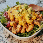 Avocado and mango salad served on a plate with grilled chicken.