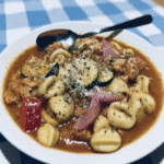 A bowl of Spicy Italian Sausage and Tortellini Soup served with a side of crusty bread and a glass of iced tea.