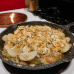 A chef's hand gently tossing the cooked potatoes with the bacon and dressing in a pot.