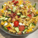 A family-style table setting with a large bowl of Chipotle Sweet Potato Pasta Salad as the centerpiece, surrounded by other complementary dishes and drinks.